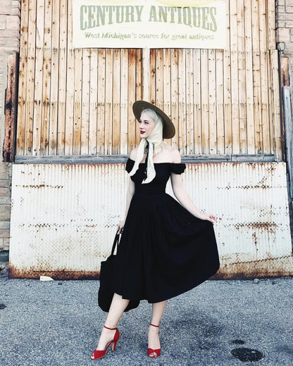 Woman in a black dress and red shoes posing in front of an 'Antiques' sign.